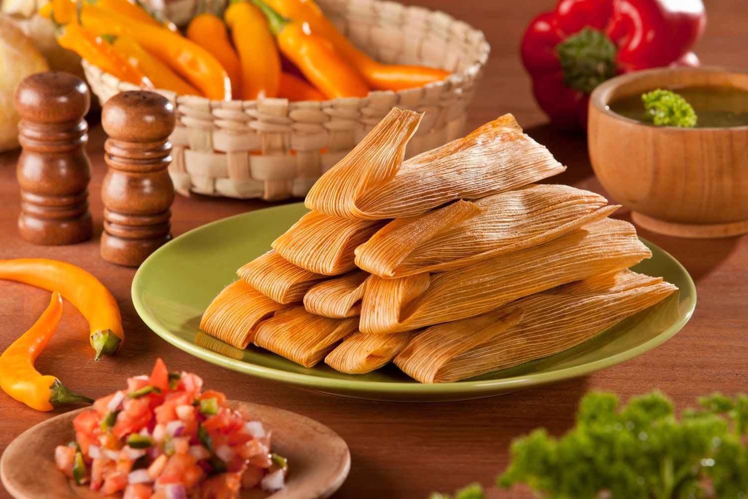 Plate of traditional tamales with fresh salsa and peppers nearby.