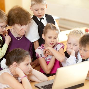 Teacher and children focused on a laptop screen in a classroom setting.
