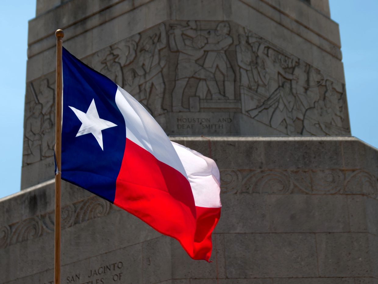 Bandera de Texas ondeando frente a un monumento.