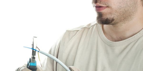 Man wearing yellow helmet cutting electrical wires with pliers.