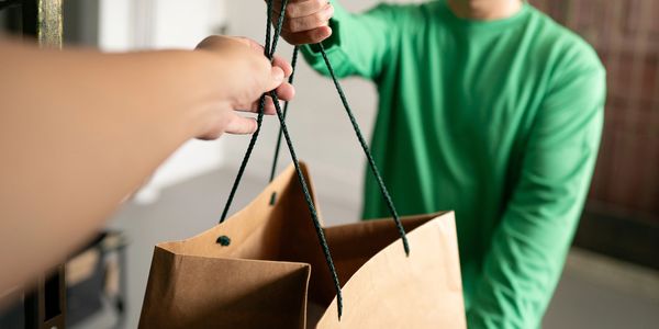 Person in green handing over a paper shopping bag.
