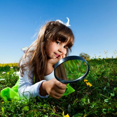 Young girl exploring nature with a magnifying glass on a sunny day.