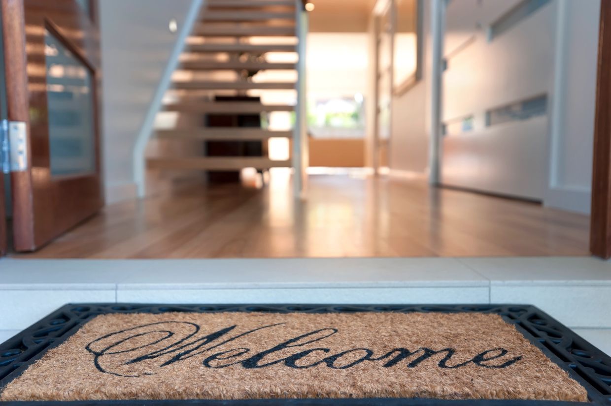 Close-up of a welcome doormat at a home's entrance with stairs inside.