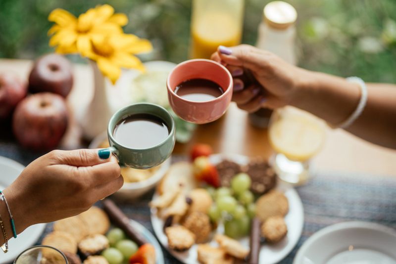 Close-up of a young couple toasting with cups of coffee while having breakfast outside on the patio of a BnB