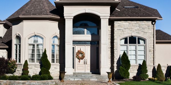 Elegant suburban house with stone facade and manicured garden under clear blue sky.