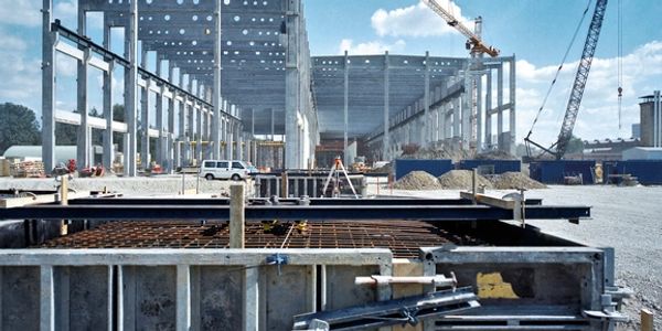 Construction site with concrete framework and cranes under a blue sky.