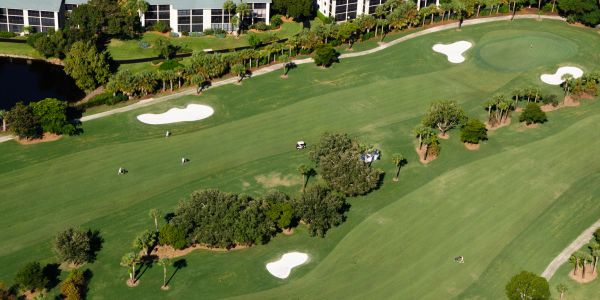 A lush golf course with sand bunkers and nearby buildings.