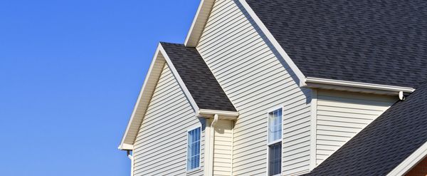 Side view of a beige house with a dark grey roof under a clear blue sky.