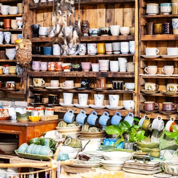 Colorful ceramic cups and bowls displayed on wooden shelves in a cozy shop.