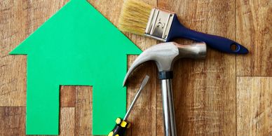 Paintbrush, hammer, screwdriver with a green house cutout on wood.