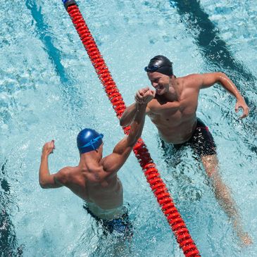 Two swimmers celebrating in a pool by bumping fists.