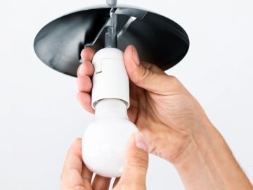 Hands installing a light bulb into a ceiling fixture.
