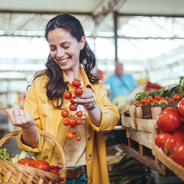 A woman holding tomatoes, smiling and looking downwards.