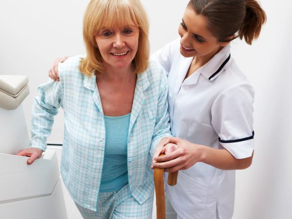 Nurse assisting elderly woman with walking at home.