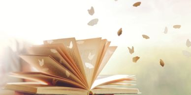 A person's hands are holding an open book. Paper butterflies are flying out of the book