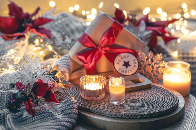 Cozy Christmas composition with a gift box, candles and a knitted element. Winter still life, Christmas celebration concept.