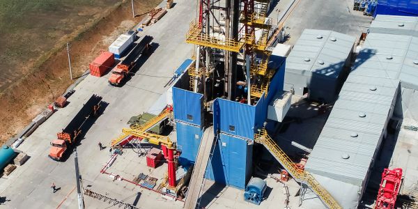 Aerial view of an oil drilling rig with surrounding equipment and vehicles.