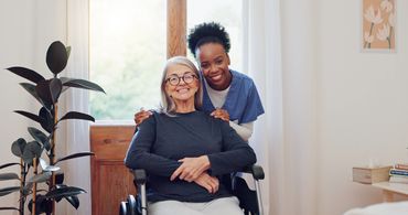 Smiling elderly woman in wheelchair with a caring nurse behind her.