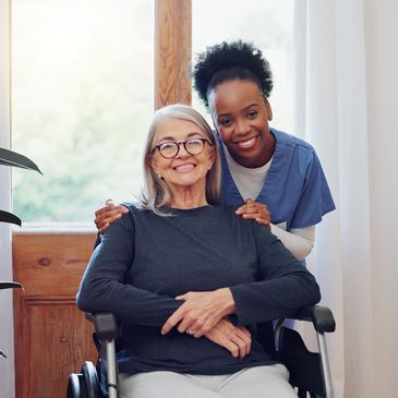 Smiling elderly woman in wheelchair with a caring nurse behind her while receiving home care services. 