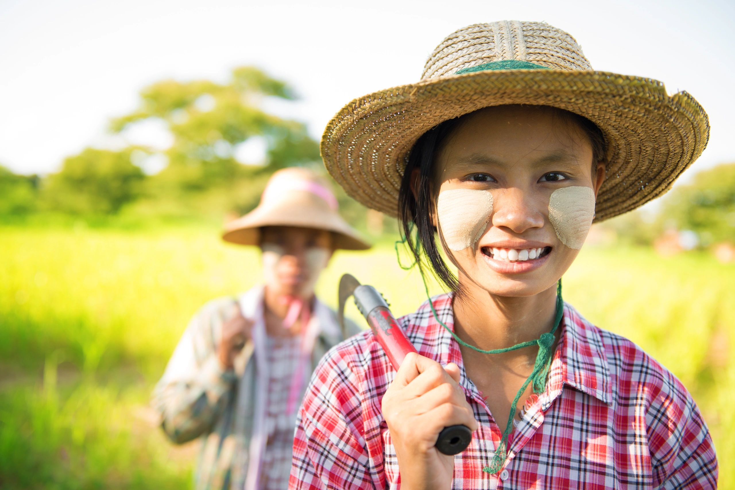 Two farmers in straw hats with traditional face paint in a sunny field.