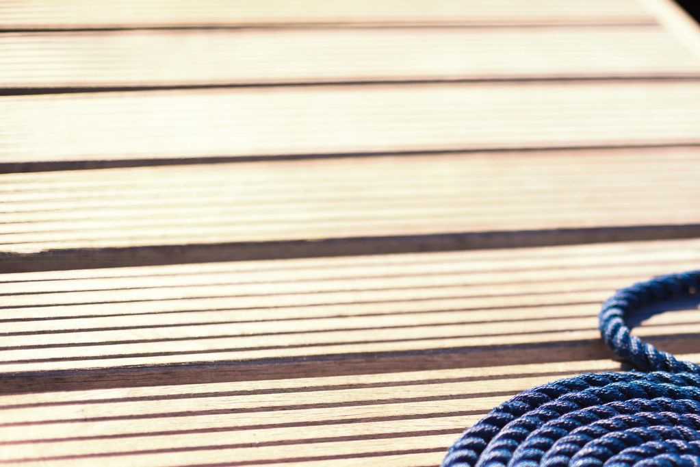 Blue rope coiled on wooden deck with striped shadows.