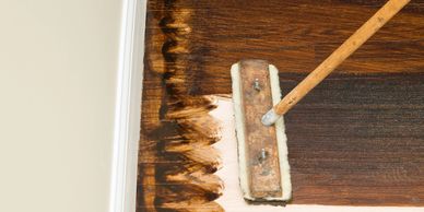 A floor being stained dark brown with a mop.