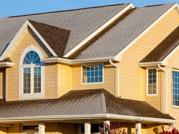 Yellow house with brown roof and white window frames.
