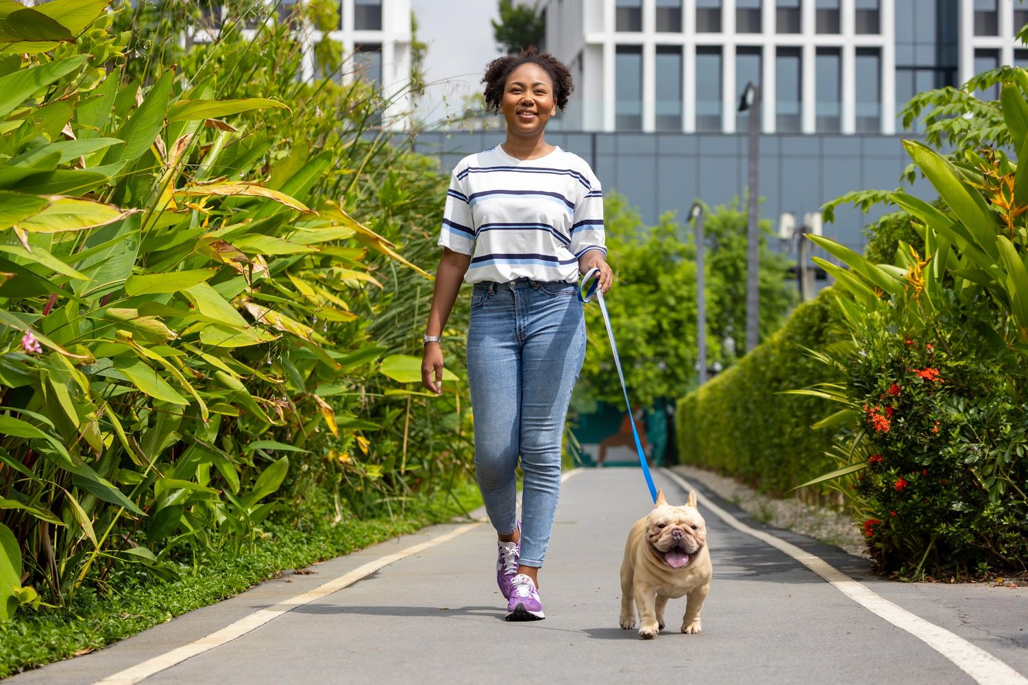 Woman walking her dog on a sunny, green pathway.