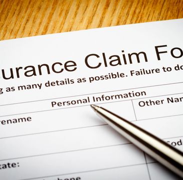 Close-up of an insurance claim form with a calculator, pen, and eyeglasses.