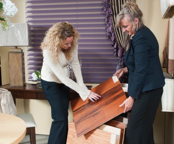 Two women examining wooden flooring samples indoors.
