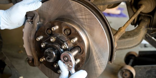 Mechanic wearing gloves repairs a car's brake system using a ratchet wrench.