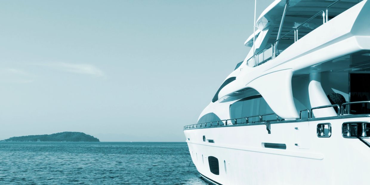 White yacht on calm blue sea near an island.