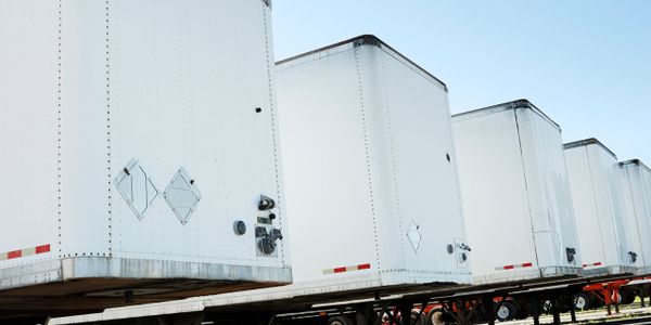 Row of white semi-truck trailers lined up under a clear sky.