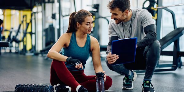 Personal trainer coaching a woman at the gym with a clipboard.