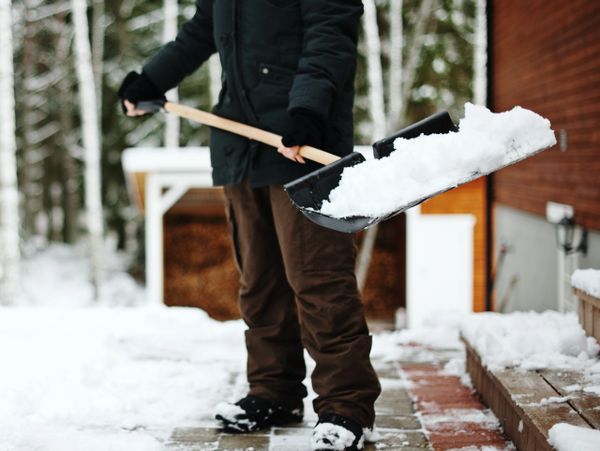 Person shoveling snow on a pathway near a house in winter.