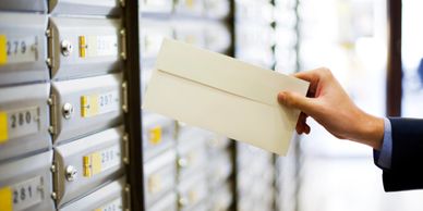 A person holding an envelope near a mailbox slot.