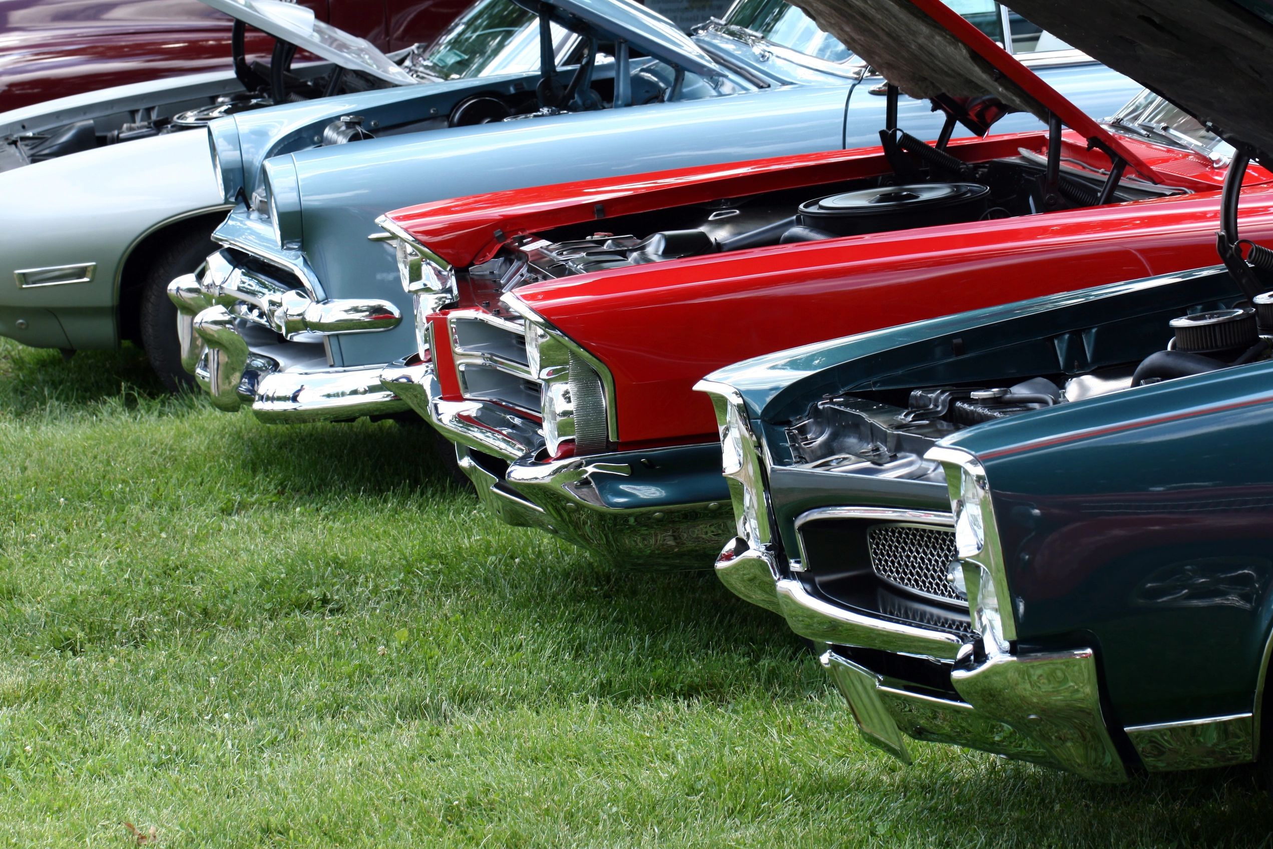Row of classic cars with hoods open at an outdoor car show