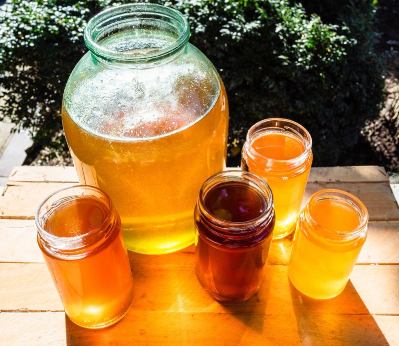 above view of different kinds of honey in various glass jars on table in backyard illuminated by sun
