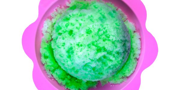 Green shaved ice in a pink flower-shaped bowl.