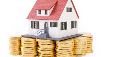 A miniature house model sitting on stacks of golden coins.