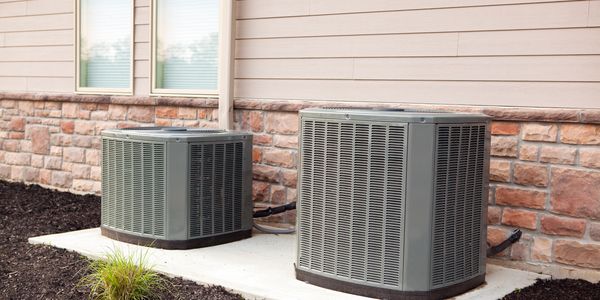 Two outdoor air conditioning units next to a house on a concrete pad.