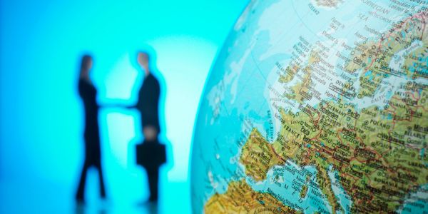Globe with Europe in focus and two blurred business people shaking hands.