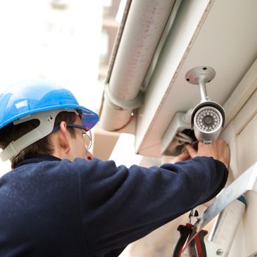 Technician installing a security camera on a building exterior.