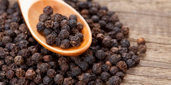 Black peppercorns in a wooden spoon.