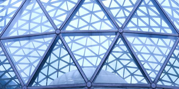 Geometric glass dome with triangular patterns reflecting sky and structures.
