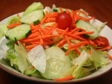 Fresh salad with cucumbers, cherry tomatoes, shredded carrots, and lettuce.