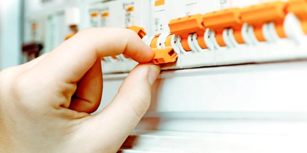 Hand adjusting an orange switch on an electrical panel.