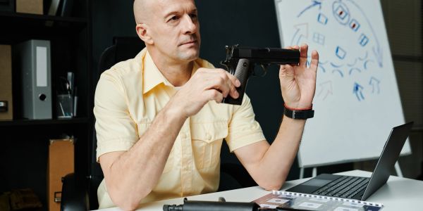Man inspecting a handgun at a desk.