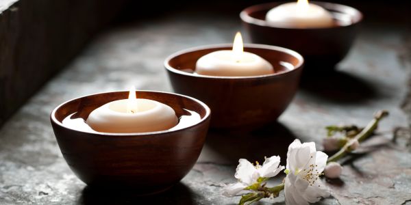 Three lit candles in bowls with white flowers nearby.