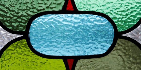 Close-up of textured stained glass with green, blue, and red sections.